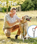 Man securing a pet tie to the ground with a smiling dog outdoors.