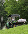 Person using 15-Gallon 12 Volt Dripless EZ Mount ATV UTV Spot Sprayer with translucent tank on utility vehicle in grassy area