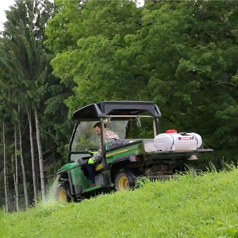 Person using 15-Gallon 12 Volt Dripless EZ Mount ATV UTV Spot Sprayer with translucent tank on utility vehicle in grassy area