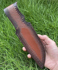 Rugged Leather Knife Sheath For Fixed Blade Knives With Secure Buckle Scabbard Pouch held outdoors on grass