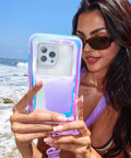 Person holding Waterproof Phone Pouch With Lanyard IP68 Floating Case For All Phones in Lavender Holo, using phone at the beach