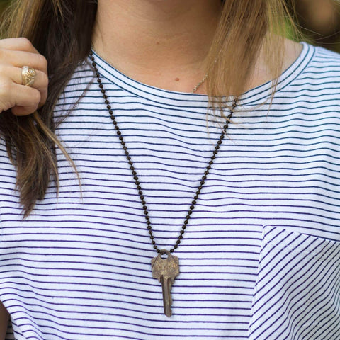 Woman wearing a bead chain necklace with a key pendant over a striped shirt.