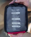 Hand holding Two Person Day Trip First Aid Kit With Bandages Gauze And Butterfly Closures For Outdoor Adventures Grab And Go Emergency Medical Kit For Hiking Camping Travel, showing contents list on the case.
