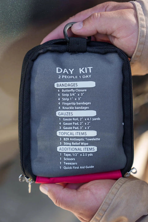 Hand holding Two Person Day Trip First Aid Kit With Bandages Gauze And Butterfly Closures For Outdoor Adventures Grab And Go Emergency Medical Kit For Hiking Camping Travel, showing contents list on the case.