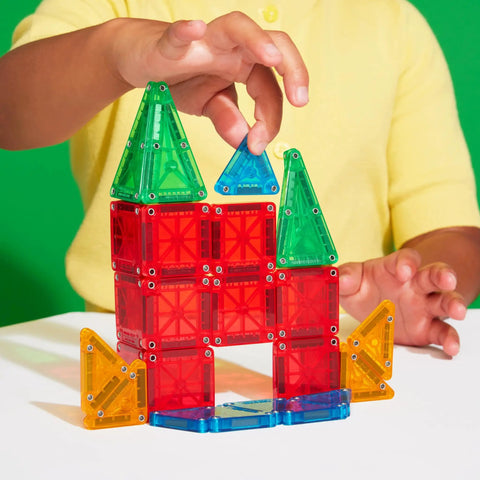 Child building with Travel Magnetic Construction Set With 26 MicroMAGS Tiles, colorful blocks on table, green background