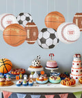 8 Pack 12 Inch Sports Paper Lanterns Set for Party Decor Includes Soccer Ball Basketball Baseball American Football and Japanese Hanging Lanterns Reusable Game Day Birthday Favors for Kids hanging over a dessert table.