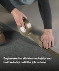 Person applying Extra Heavy Duty Olive Duct Tape 6969 on carpet edge, demonstrating industrial strength and water-resistant bond