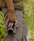 Person holding camera with Micro Clutch I Plate Hand Strap for Mirrorless Cameras with Low Profile Finger Loop Battery Access