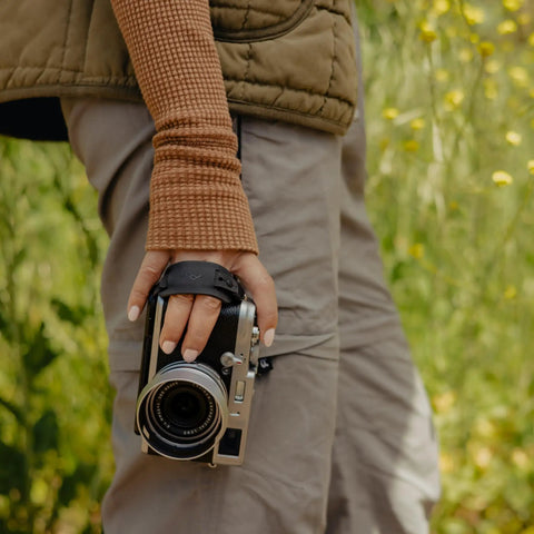 Person holding camera with Micro Clutch I Plate Hand Strap for Mirrorless Cameras with Low Profile Finger Loop Battery Access