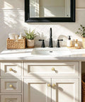 Three Pack 1 1/4 Inch Brushed Gold Solid Zinc Cabinet Knobs on white bathroom vanity under black-framed mirror