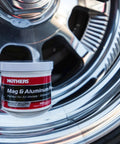 Mag And Aluminum Metal Polish That Restores Dull Surfaces To A Showroom Shine Easy Buff Perfect For Aluminum Stainless Steel Brass Chrome And More 5 Oz Jar next to shiny chrome wheel.