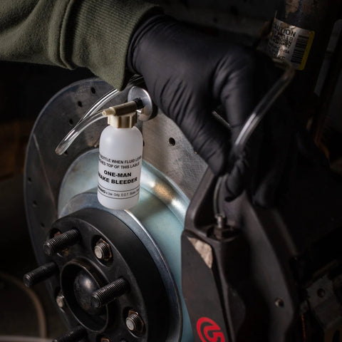 One-Man brake bleeder bottle with clear hose attached to car brake caliper near rotor