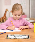 Child writing at desk with 40 Pack Clear Self Adhesive Nameplate Pockets For Desks 10.5 By 3.5 Inches; giraffe toy in background.