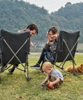 Oversized Folding Rocking Camping Chair With Padded Comfort Portable Rocker For Patio Lawn And Outdoors Heavy Duty Armchair Supports Up To 400 Lbs Gray For Adults being used outdoors by a family with a toddler and dog.