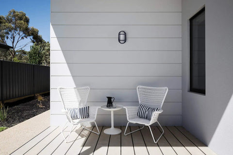 Patio setup with chairs and table beneath Outdoor 10 Point 6 Inch Oval LED Nautical Bulkhead Light Flush Mount on wall.