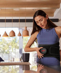 Woman using Venom 2 Back Wrap With Next Level Heat And Vibration For Fast Pain Relief Soreness And Inflammation, in a kitchen setting