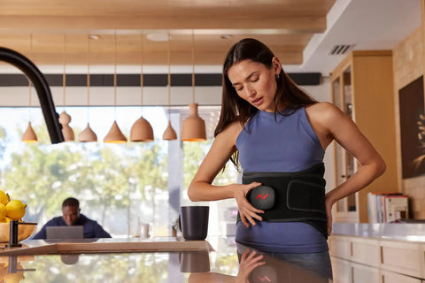 Woman using Venom 2 Back Wrap With Next Level Heat And Vibration For Fast Pain Relief Soreness And Inflammation, in a kitchen setting
