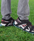 Person wearing Lawn Aerator Sandals Spiked Shoes For Yard Work on grass, showing 3 straps and iron spikes.