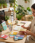Woman writing in 24 Pack Mini Journal Notebooks With Ballpoint Pen, Themed Composition Notebooks For Back To School And Office Supplies.