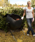 50 Gallon Compost Tumbler in black with open lid, standing in garden next to person. Rotates effortlessly to speed up composting.