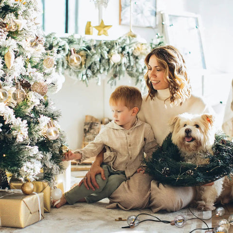 Woman and child decorate Christmas tree with Indoor 2 Pack G50 LED String Lights With Vintage Filament Bulbs, dog with wreath nearby.