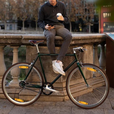 Man sitting on stone railing holding coffee next to bike with 4 Pack Bicycle Wheel Spoke Reflectors For Front And Rear Mountain Bike Safety