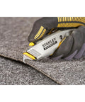 Hand holding 2 In 1 Snap Off Knife Xtreme with 9mm blade cutting grey material, stainless steel blade guide visible