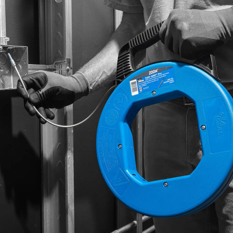 Person using Sturdy 100 ft Stainless Steel Fish Tape With Metal Eyelet Tuff Grip Pro Case For Wet Environments And Tight Bends Nylon Jacketed Pulling Tool Built For Easy Wire Runs indoors.