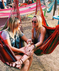 Two women smiling sitting in colorful hammock chairs outdoors; image for Hammock Chair Hanging Rope Swing Seat For Indoor And Outdoor Use Sturdy Cotton Weave Cozy Chill Lounge Swing Supports Up To 300 Lbs Easy Hanging Setup Gray.