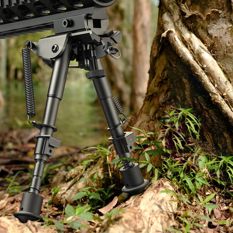 6 To 9 Inch Picatinny Bipod With Adjustable Five Setting Legs And Spring Return Quick Attach Picatinny Adapter Included Heavy Duty Steel And Aluminum Construction Black Anodized Finish For Rugged Hunting And Shooting among forest greenery.
