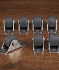 Eight Piece Low Profile Rigid Rubber Caster Wheels Non Swivel Fixed Plate Casters with grey wheels on a wooden surface.