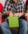 Person holding a green bag from 24 Pack Small Gift Bags With Handles Rainbow Colors 8.3 By 6 By 3.15 Inch Heavyweight Paper Bags