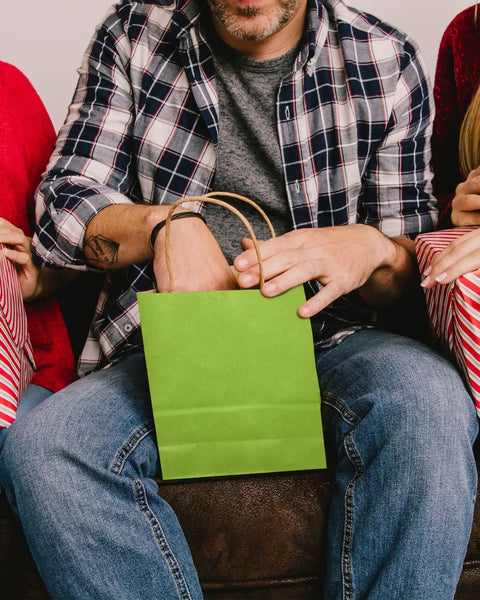 Person holding a green bag from 24 Pack Small Gift Bags With Handles Rainbow Colors 8.3 By 6 By 3.15 Inch Heavyweight Paper Bags