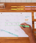 Hand using Pocket Highlighters In Soft Pastel Assorted Colors, 12 Count, Slim Chisel Tip for organizing a calendar with notes.