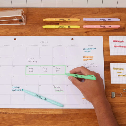 Hand using Pocket Highlighters In Soft Pastel Assorted Colors, 12 Count, Slim Chisel Tip for organizing a calendar with notes.