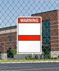 Warning sign on chain-link fence in front of a brick building