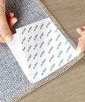 Hands peeling rug tape to apply Anti Slip Rug Tape For Hardwood Floors 12 Pack Rug Grips White Rug Stickers to carpet edge.