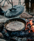 Heavy Duty Dutch Oven Lid Lifter with Coil Handle lifting lid over campfire, durable steel tool for safe lifting of hot lids, prevents scalding.