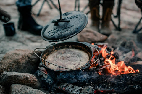 Heavy Duty Dutch Oven Lid Lifter with Coil Handle lifting lid over campfire, durable steel tool for safe lifting of hot lids, prevents scalding.