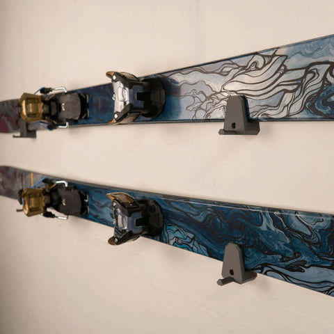 Slick Horizontal Ski Rack Wall Mount Bracket Black Hookless Design keeps skis flat against wall with blue topsheet pattern.