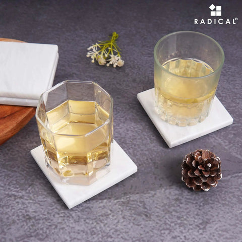 Solid White Square Marble Coasters Set Of Six, Polished Drink Pads for two glasses on a table with decorative items.