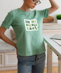 Person wearing a light green t-shirt with 'In My Pickle Era' text, in a kitchen setting, with a calm and neutral expression.