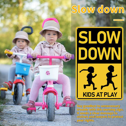 Two children on tricycles next to a Slow Down Kids At Play Road Sign For Neighborhoods, Aluminum Weatherproof Safety Plaque.