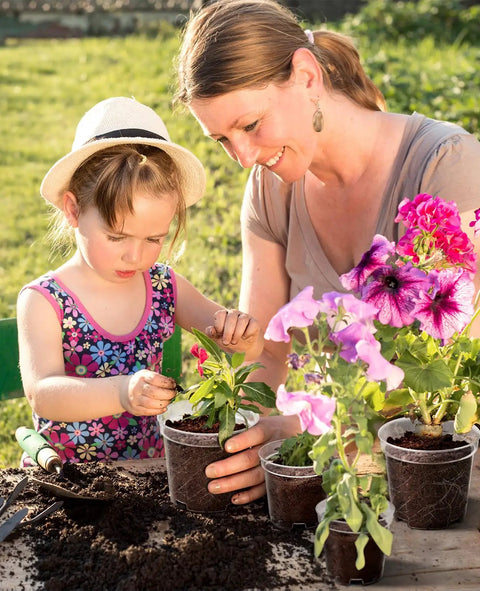 Child and adult planting flowers in clear 4 inch plant pots with drainage holes in garden, highlighting DIY seed starter use.