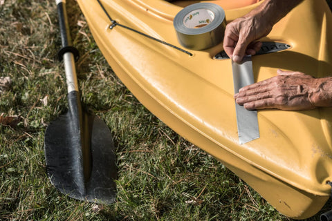 Duck Brand duct tape being applied to a yellow kayak; silver repair tape visible.