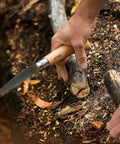 Badass Lightweight Folding Saw For Weekend Campouts And Garden Grind Cuts Branches Fast With Razor Sharp Carbon Steel Blade Secure Virobloc Lock And Natural Beechwood Handle in hand cutting a branch.