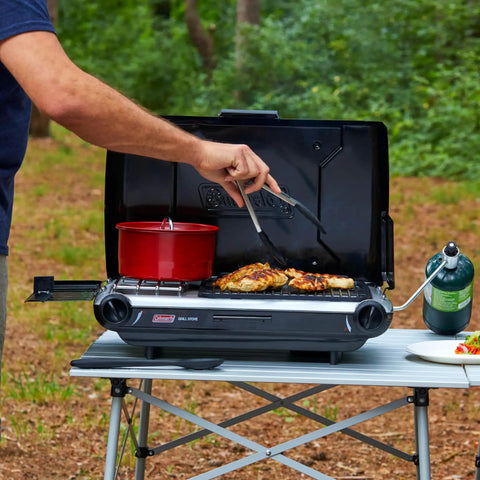 Person using 2-In-1 Tabletop Camping Grill And Stove With Two Burners, 20,000 BTUs Of Cooking Power, cooking chicken outdoors.