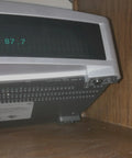 Silver stereo system displaying FM 97.7 on wooden shelf