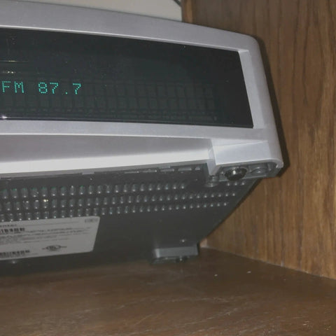 Silver stereo system displaying FM 97.7 on wooden shelf