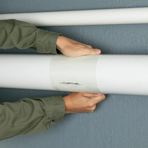 Hands applying Ultra Strong Waterproof Tape That Seals Leaks On Wet Surfaces And Underwater, Clear 8 Inch By 25 Foot Roll on pipe